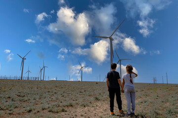 A boy and a girl hold hands and look at the wind turbine. Concept Children look to the future