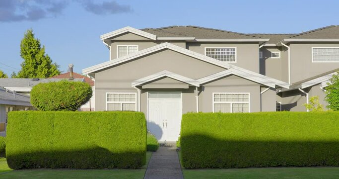 Establishing shot of two story stucco luxury house with garage door, big tree and nice landscape in Vancouver, Canada, North America. Day time on June 2021. ProRes 422 HQ.