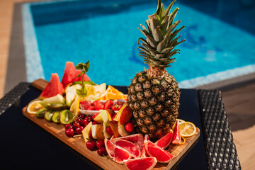 Plate of tropical fruits: watermelon, pineapple, bananas, mangosteen, passion fruit, mango and dragon fruit by the pool