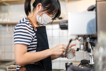 Asian Barista girl wear mask, use grinder machine make coffee in cafe.