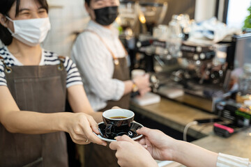 Fototapeta na wymiar Asian waiter wear mask, handing cup of hot coffee to customer in cafe. 