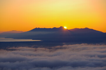 快晴の空に眩しく輝く朝陽に照らされた雲海とシルエットの際立つ遠くの山。