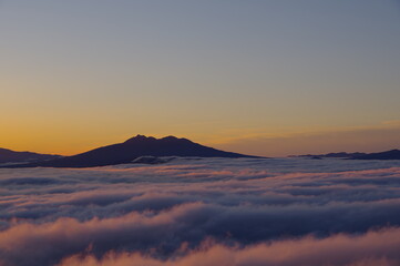 Fototapeta na wymiar ダイナミックに広がる雲海と夜明けの空に浮かぶ遠い山のシルエット。