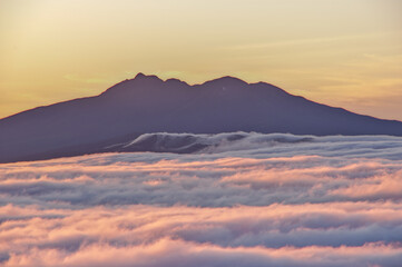 ダイナミックに広がる雲海と夜明けの空に浮かぶ遠い山のシルエット。
