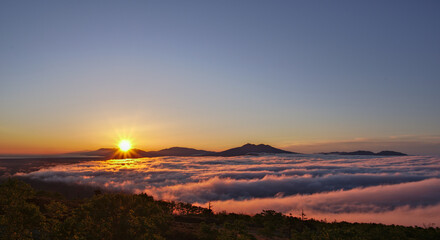 快晴の空に眩しく輝く朝陽に照らされた雲海とシルエットの際立つ遠くの山。