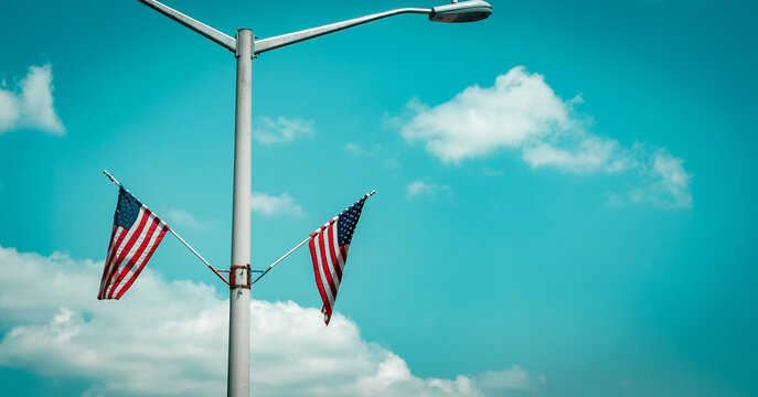 America USA flags on a light post with blue cloudy skies