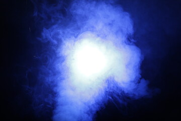 Artificial magic smoke in blue light on black background
