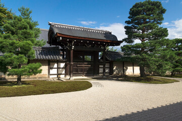 Fototapeta premium Sunlit stone zen garden with raked gravel an gate at Sogenchi garden at Tenryu-ji temple in Kyoto, Japan