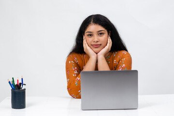 Portrait of a tired young Indian girl resting her chin in her palms as she sits infront of her...