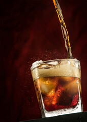 Pouring cola from bottle into glass with splashing.