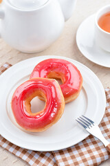 Close up Strawberry Donut on a white plate with a cup of coffee in the background