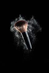 Make-up brush with white powder explosion on black background