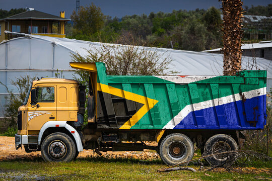 Dump truck with the image of the national flag of South African Republic is parked against the background of the countryside. The concept of export-import, transportation, national delivery of goods