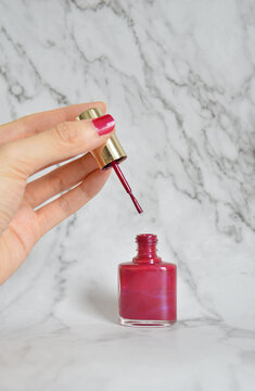 Cropped Hand Holding A Brush Cap Of A Hot Pink Nail Polish Bottle In Marble Background