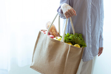 エコバッグに入った野菜やパンを持つ女性の手元