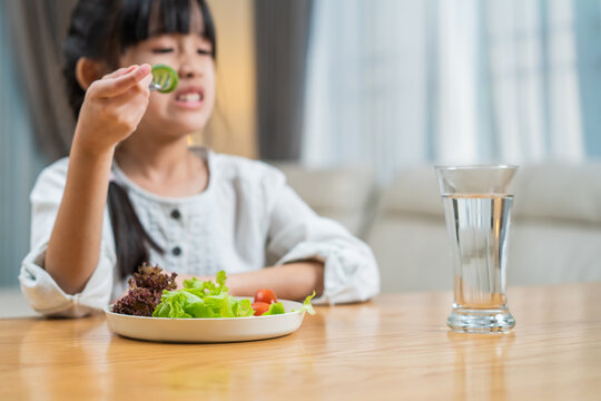 Unhappy Asian girl child don't want to eat vegetables on dinner plate.