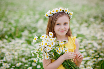 A girl in a yellow T-shirt on a blooming field of daisies with a bouquet in her hands and a wreath...