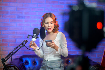 Fototapeta na wymiar Young smiling female singer wearing headphones with a microphone while recording song in a music studio with colorful lights.