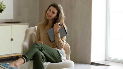 Obraz premium Happy young woman using digital tablet, sitting on sofa, smiling and holding pc computer.