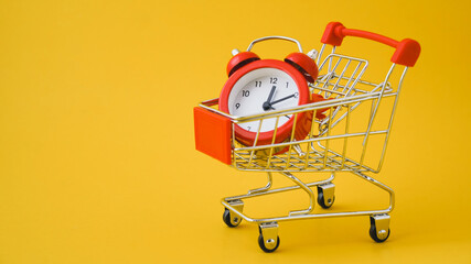 red analog clock on shopping cart with yellow background , payday ,shopping day or sale promotion...