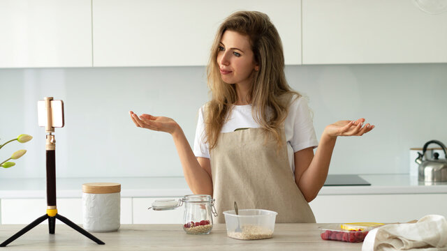 Food video blogger wearing apron makes a video using phone on tripod. Social media influencer creating content.