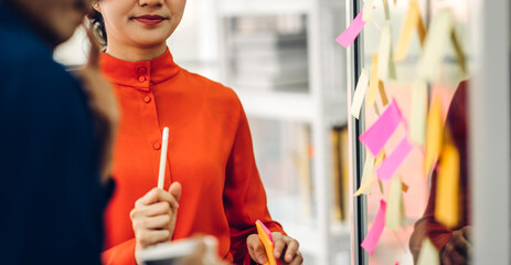 Casual creative happy two smile asian business people planning strategy analysis and brainstorm putting post it stickers note to share idea for startup project on glass board at modern office