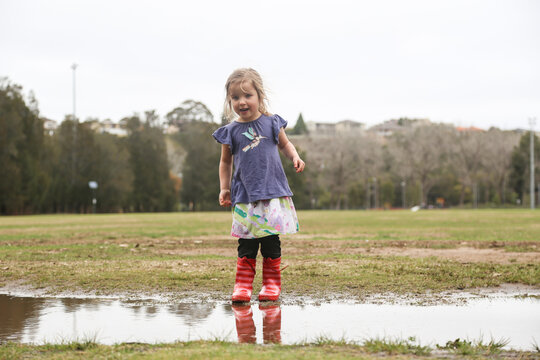 Young girl wearing red gumboots playing in puddles