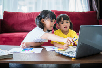 Two asian child girl students study online with teacher by video call together. Siblings are homeschooling with computer laptop during quarantine due to Covid 19 pandemic.
