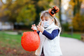 Little toddler girl dressed as a witch with medical mask on face trick or treating on Halloween....