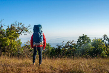 Young traveler wearing red sweater and green backpack standing and watched beautiful view on top of the mountain. He is happy to be with herself and stay with nature.