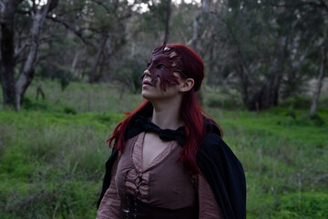 portrait of red haired girl wearing fantasy medieval clothes of a wandering adventurer.  natural light in a woodland forest setting.