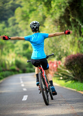 Woman no handed cycling on tropical park trail in summer