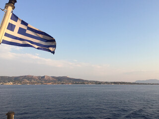 The Greek National Flag flies at the stern of a ferryboat over the Aegean Sea in the vicinity of the island of Aegina, Greece.