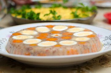 Aspic meat jelly on a white plate close-up, decorated with chicken eggs and carrots in the form of flowers