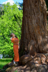 Trendy woman in orange outfit standing looking up into a tree
