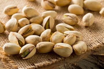 Heap of salted, roasted green pistachio nuts snack on burlap sack background, healthy food snack