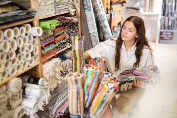 Fototapeta premium Young attractive housewife touching and choosing cotton carpets in interior shop