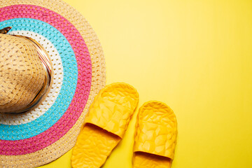 Top view of woman summer hat and slippers on yellow background.