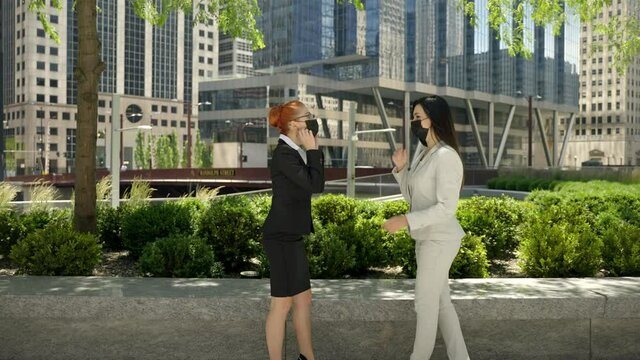 Two young Caucasian female busness women in face masks approaching each other, taking face masks off and shake hands.