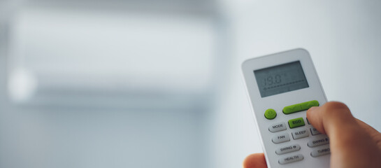 Close-up of male hand using remote control of split air conditioner. Panoramic banner with copy space.