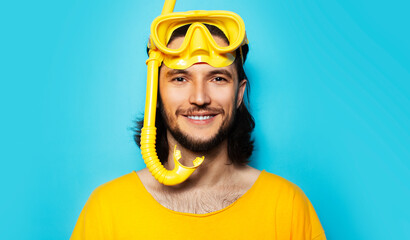 Portrait of young smiling man in yellow wearing diving googles and snorkel on blue background.