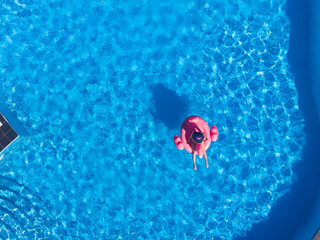 woman on flamingo pool float in pool, drone aerial view. Summer holidays
