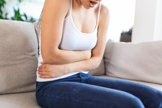 Woman lying on sofa looking sick in the living room. Beautiful young woman lying on bed and holding hands on her stomach. Woman having painful stomachache on bed, Menstrual period