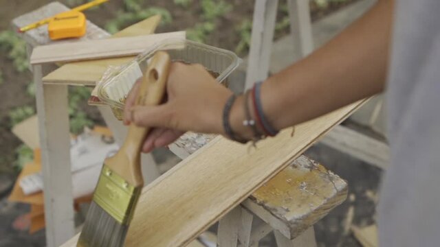 woman varnishing wood planck with brush. slow motion