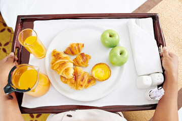 Maid carrying tray with breakfast to hotel room, it consist of fresh croissants, apples, and...