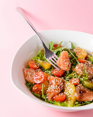 Fresh salad with shrimp and vegetables close up in a bowl over pastel pink background.
