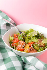 Fresh salad with shrimp and vegetables close up in a bowl over pastel pink background.