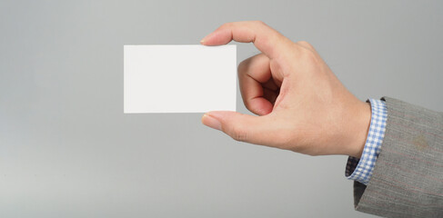 Hand is holding white blank card and wear suit on gray background. business man concept