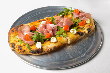 Pinza with vegetables and meat cooked in an oven with wood and served on a metal tray over white background.