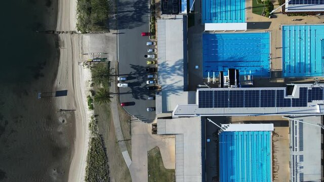 Unique view looking down at an Olympic pool complex built next to a coastal city pathway. High drone view
